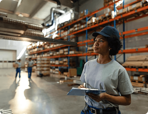 Warehouse worker reviewing inventory on a clipboard among storage shelves