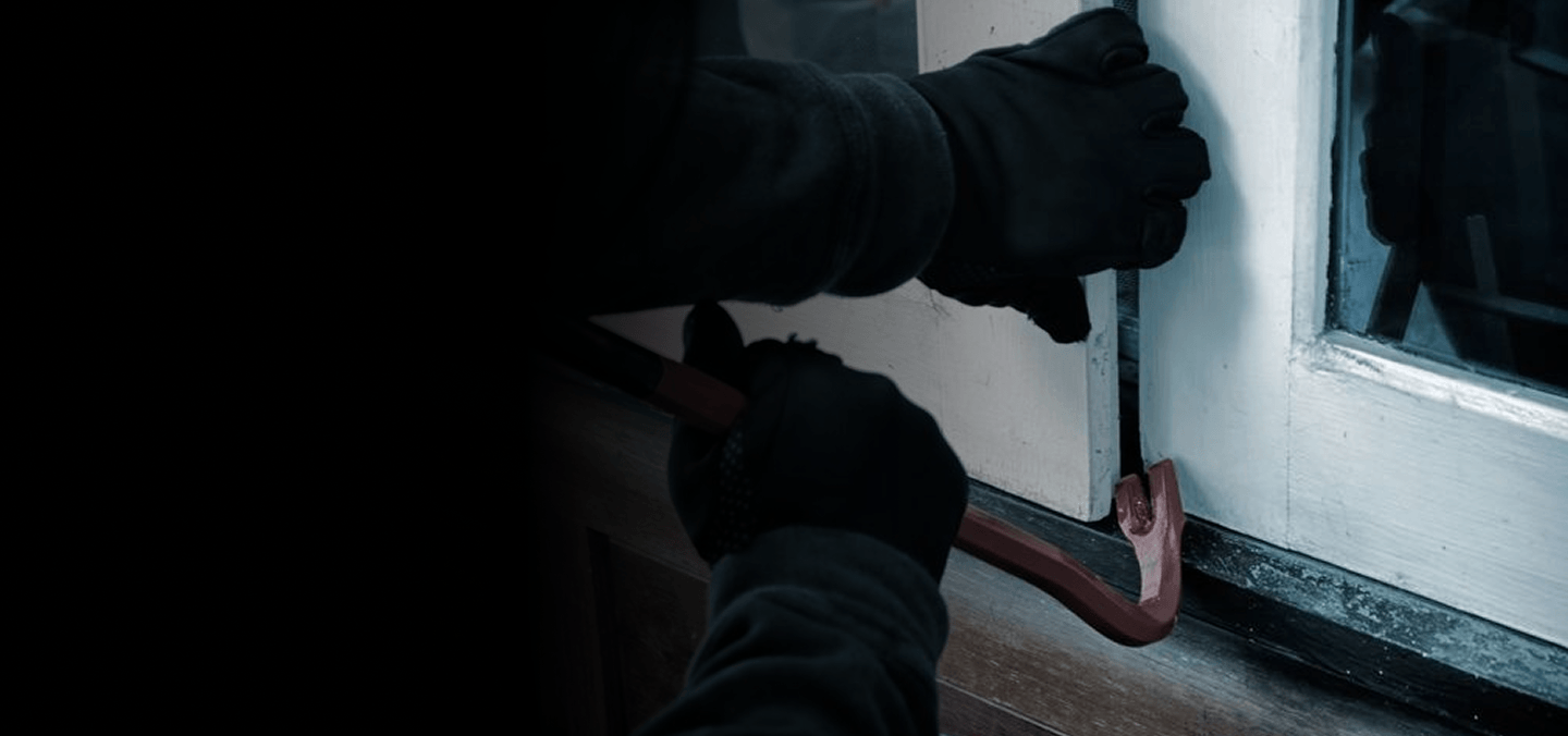 Gloved hands prying open a window with a crowbar