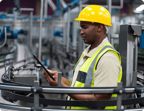 Factory worker in a hard hat and safety vest reviewing a clipboard
