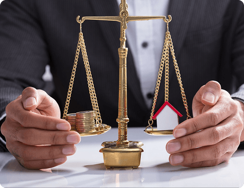Scales of justice on a desk beside a coin stack and small house model