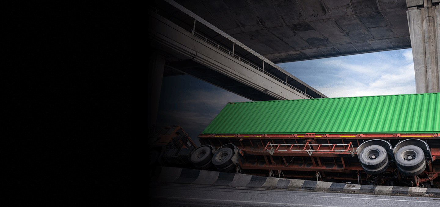 Overturned truck carrying a green tarped load under a bridge