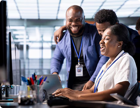 Colleagues gathered around a desk smiling at a computer screen